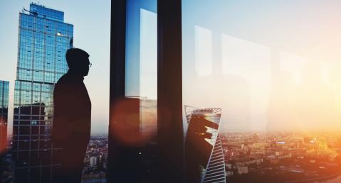Silhouette of a person in the office looks far over the city