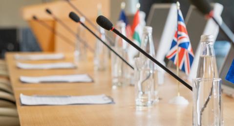 Long negotiating table with microphones, clipboards, water bottles and country flags