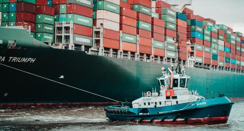 a tugboat crosses a large container ship