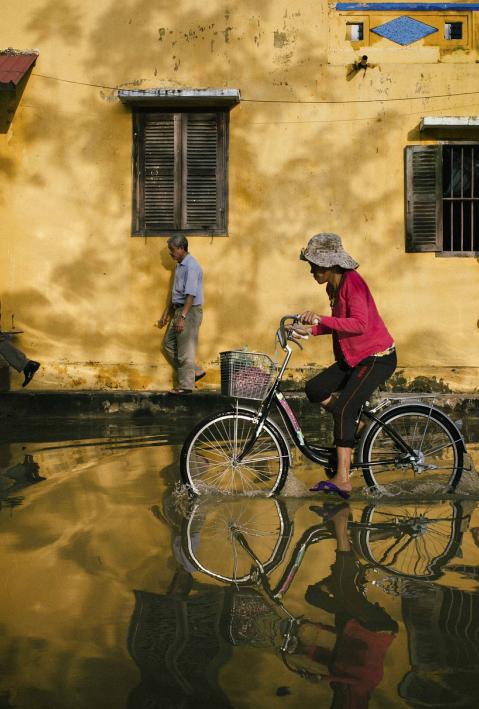 Flooded street through which a person is riding a bicycle. 