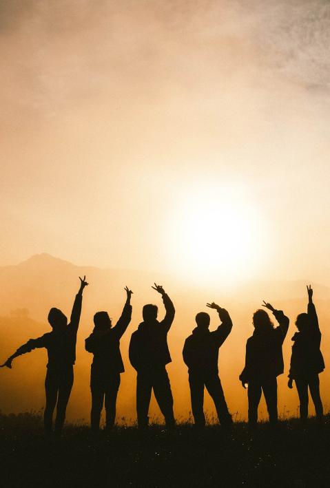 Silhouetten von Menschen auf einem Berg die die Sonne gr&uuml;&szlig;en