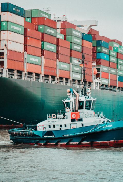 a tugboat crosses a large container ship