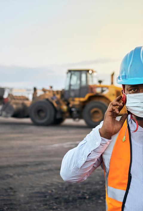 Miner with helmet and safety waistcoat in front of an excavator