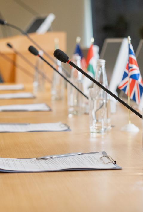 Long negotiating table with microphones, clipboards, water bottles and country flags