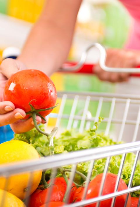 Full shopping cart at store with fresh vegetables and hands close-up