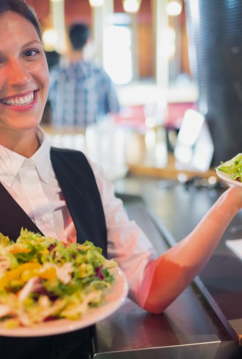 Pretty barmaid holding plates of salads in a bar