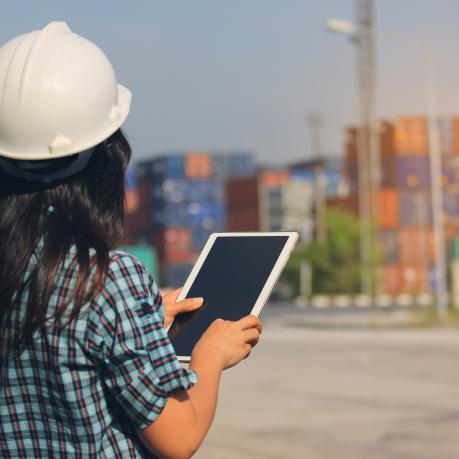 Person mit Helm und Tablet schaut auf Container in der Ferne