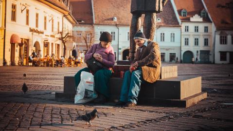&Auml;lteres P&auml;rchen sitzt am Sockel einer Statue und trinkt Cola auf einem Marktplatz in Sibiu, Rum&auml;nien