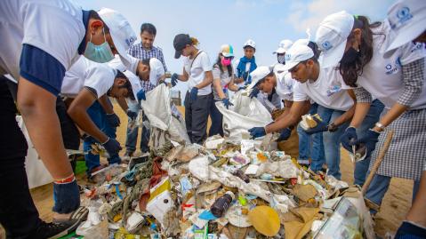 People standing around a big pile of trash, cleaning it up