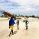 A man and two kids are carrying woods on the beach of Mozambique. 